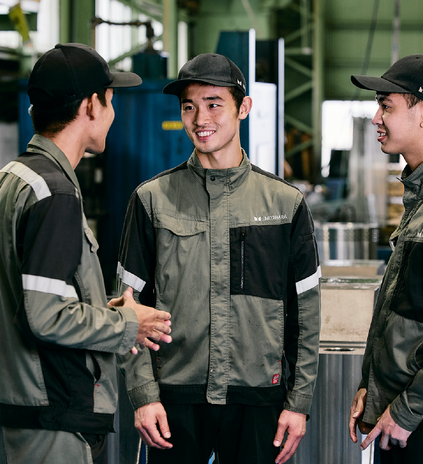 作業服を着た3人の工場スタッフが笑顔で会話している様子